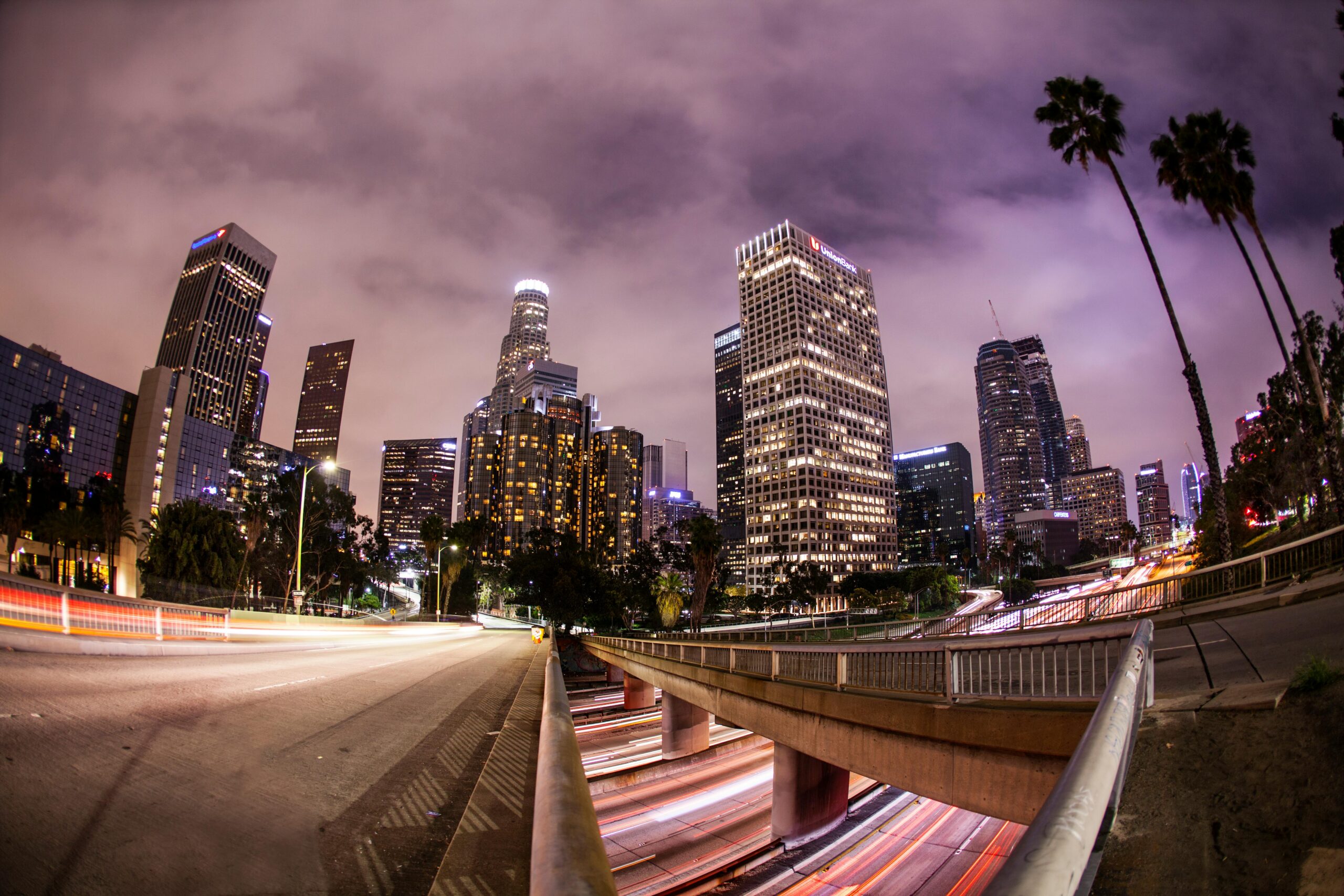Long exposure of bustling downtown Los Angeles skyline with light trails, showcasing urban architecture at night.